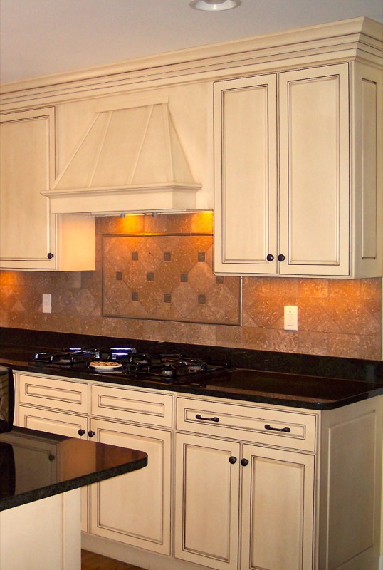 Stone tile backsplash set on the diagonal beneath cream glazed cabinets