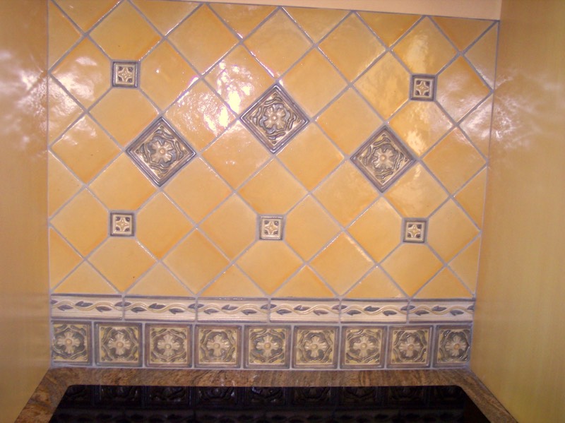 Gold glazed tile backsplash with decorative relief inserts and a border
