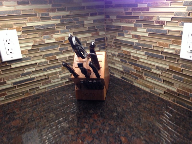 Linear glass and slate mosaic backsplash meeting a granite countertop