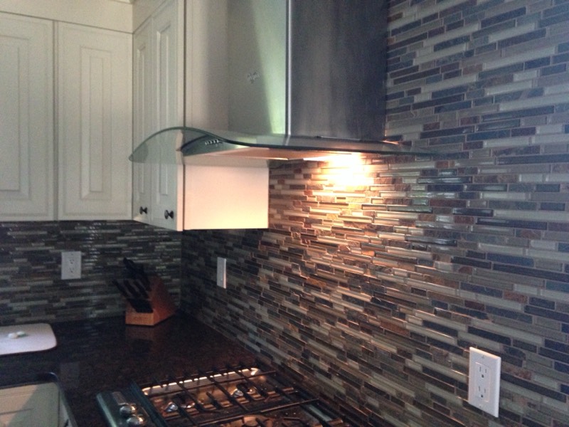 Glass and stone mosaic backsplash behind a gas range and stainless hood