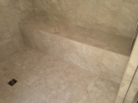 Travertine shower with a built-in bench and mosaic tile floor