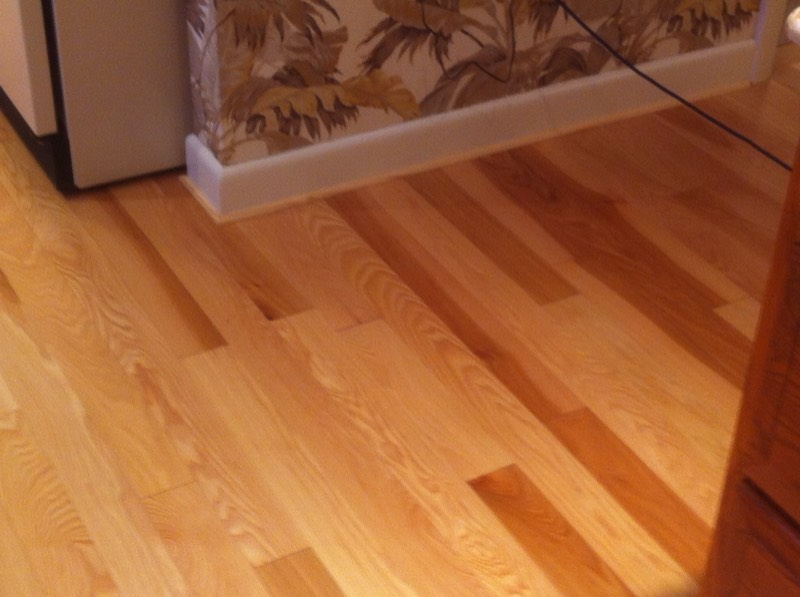 Natural finish oak hardwood flooring beside white baseboard